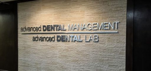 metal faced acrylic sign in brushed aluminum on black acrylic mounted for advanced dental interior lobby stone wall