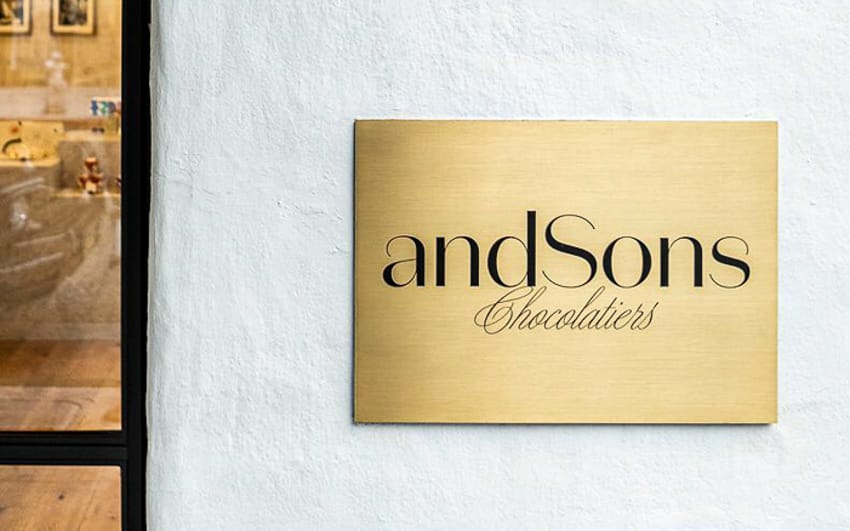 Brushed brass fabricated letters for And Sons Chocolatiers on an exterior facade