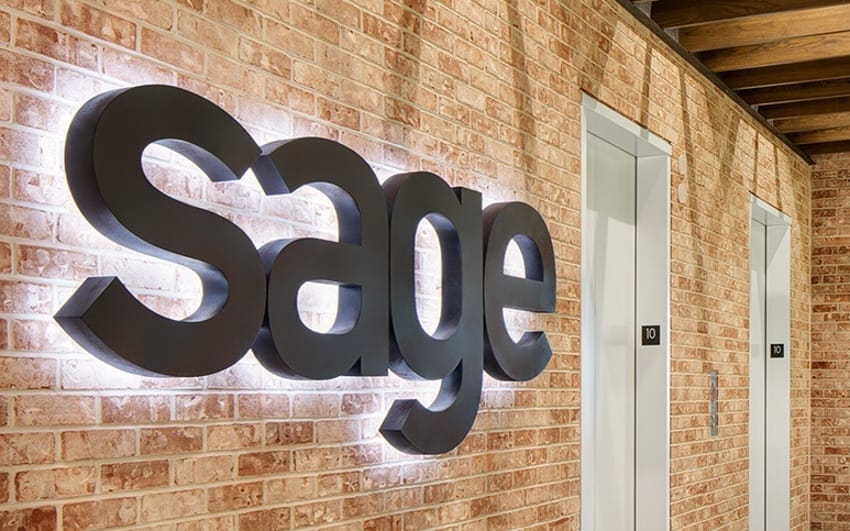 Matte black halo-lit backlit metal letters with natural white LEDs on a brick office lobby wall — Sage