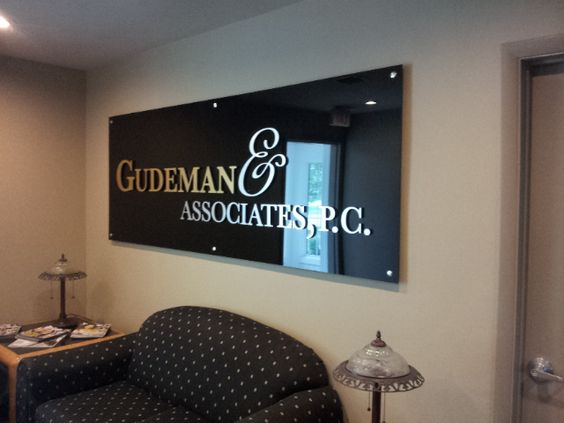 Metal-laminate logo on a black acrylic panel sign — Gudeman office lobby