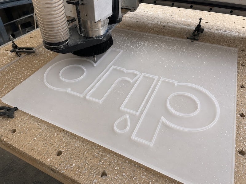 CNC router cutting the Drip letterforms out of a white acrylic sheet for a push-through sign