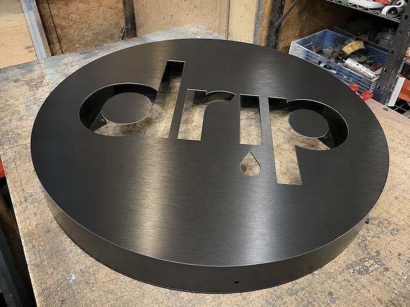 Brushed black aluminum cabinet with the Drip logo routed out, on the shop bench before the acrylic is fitted
